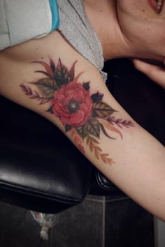 a woman's arm with a red flower and leaves tattoo on her left arm