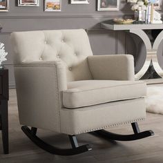 a gray rocking chair in a living room with pictures on the wall and flooring