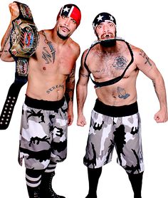 two men with tattoos and wrestling gear standing next to each other, one holding a wrestler's belt