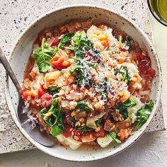 a bowl filled with pasta and vegetables on top of a table next to a glass of olive juice