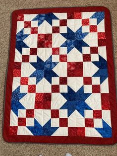 a red, white and blue quilt on the floor next to a pair of shoes