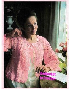 a woman wearing a pink crochet sweater sitting next to a vase with flowers