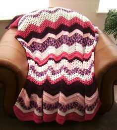 a crocheted blanket sitting on top of a brown leather chair next to a window