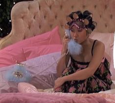 a woman is sitting on her bed talking on the phone while wearing a pink dress