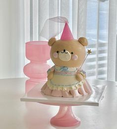 a teddy bear in a dress and hat on a cake stand with pink vases behind it