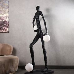 a black statue with three white balls on it's feet and one standing in front of a couch