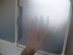 a person's hand reaching out from behind a window with frosting on it