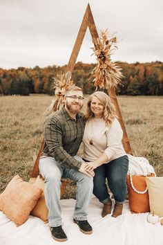 a man and woman sitting on a blanket in front of a teepee with fall decorations