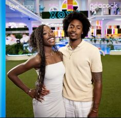 a man and woman standing next to each other in front of a building with a pool