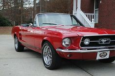 an old red mustang is parked in front of a brick building with stairs and trees