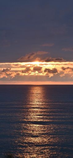 the sun is setting over the ocean with clouds in the sky and water below it