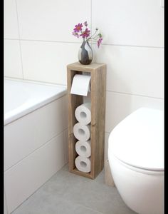 a white toilet sitting next to a wooden stand with rolls of toilet paper in it