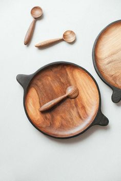 two wooden bowls and spoons on a white surface with some wood utensils