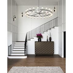 a white room with stairs and a chandelier above the entrance table, in front of a staircase