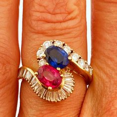 a woman's hand with two different colored stones on it and an engagement ring