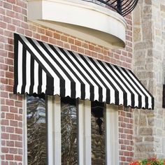 a black and white striped awning on the side of a brick building next to flowers