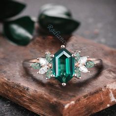 an emerald colored ring with three white diamonds on top of a piece of wood next to some green leaves