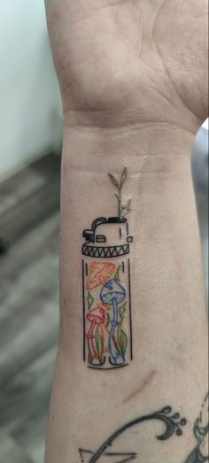 a person with a tattoo on their wrist holding up a small jar filled with flowers