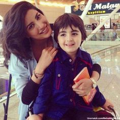 a woman holding a small boy in her arms at an airport terminal, with the child smiling for the camera