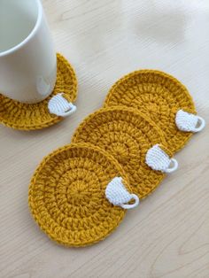 three crocheted coasters with coffee cups on them sitting next to a mug