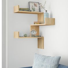 three wooden shelves on the wall above a blue couch with a clock, vase and other items