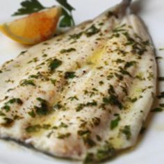 a white plate topped with fish and garnish next to a slice of orange