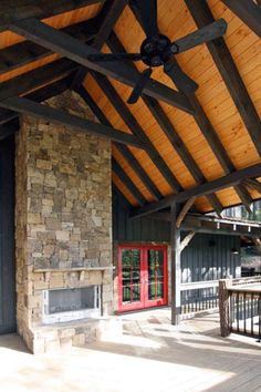 an outdoor covered patio with a ceiling fan and stone fire place in the center, surrounded by wood planks