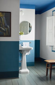 a bathroom with blue and white walls, wood flooring and a pedestal sink in the corner