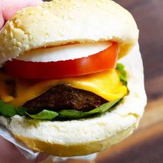 a hand holding a hamburger with cheese, tomato and lettuce