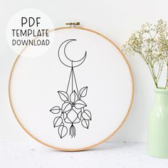 an embroidery pattern with flowers and a crescent hanging from it's hoop next to a green vase