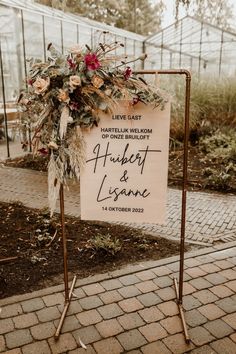 a sign that is on the side of a road with flowers and foliage around it