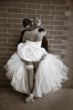 a woman in a white dress is leaning against a brick wall with her back to the camera