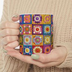 a woman holding a colorful coffee mug with crochet designs on it's sides