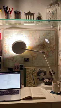 an open laptop computer sitting on top of a desk next to a book and lamp