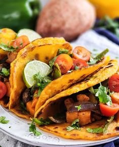 three tacos on a plate topped with vegetables and cilantros next to potatoes