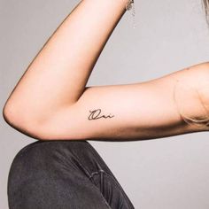 a woman with a tattoo on her arm sitting down and looking off to the side