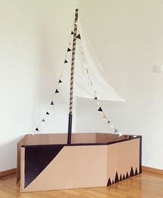 a cardboard boat sitting on top of a hard wood floor next to a white wall