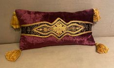 a purple and gold pillow with tassels on the sides sitting on a couch