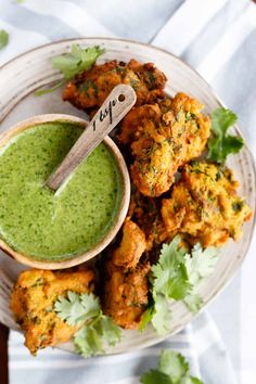 a white plate topped with fried food next to a cup of green sauce