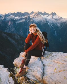 a woman sitting on top of a rock with mountains in the background