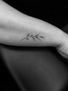 a black and white photo of a person's arm with a small branch tattoo on it