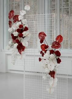 two white and red vases with flowers hanging from the ceiling in front of windows