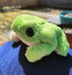 a green stuffed animal sitting on top of a person's lap in the sun