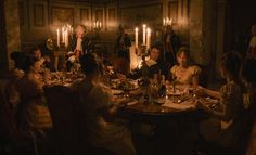 a group of people sitting around a dinner table with candles on the wall behind them