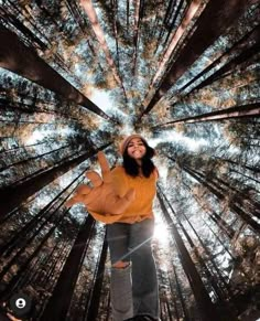 a woman standing in the middle of a forest looking up into the sky with her arms outstretched