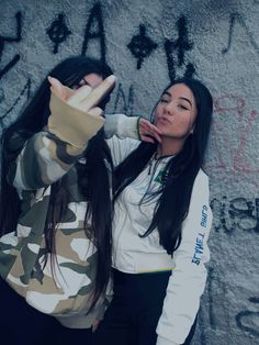 a woman standing in front of a wall with graffiti on it's walls and holding her hand up to the side