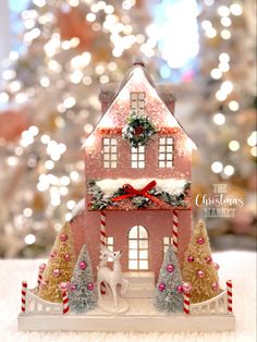 a small christmas house on a table with a tree in the background