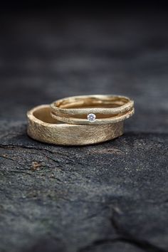 two gold wedding rings sitting on top of a stone slab with a diamond in the middle