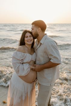 a pregnant couple standing next to each other on the beach in front of the ocean