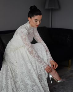 a woman in a white dress and high heels sitting on a couch with her legs crossed